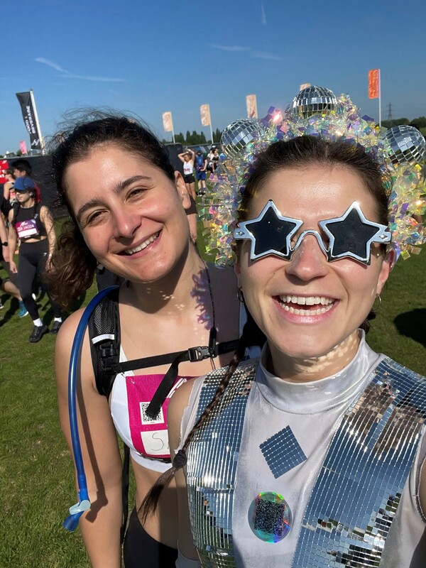 two women in a field one in shiny disco ball outfit with star shaped sun glasses 