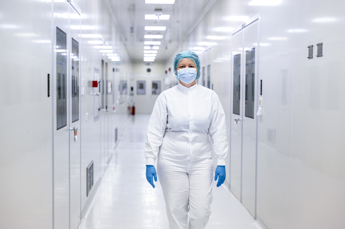 A person dressed in cleanroom clothing and a mask walking down a corridor