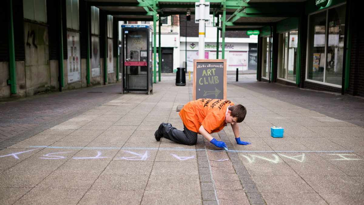 Young person using chalk on pavement. Urban wilderness.