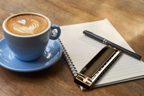 Photo of coffee cup, harmonica, pen and notepad on table