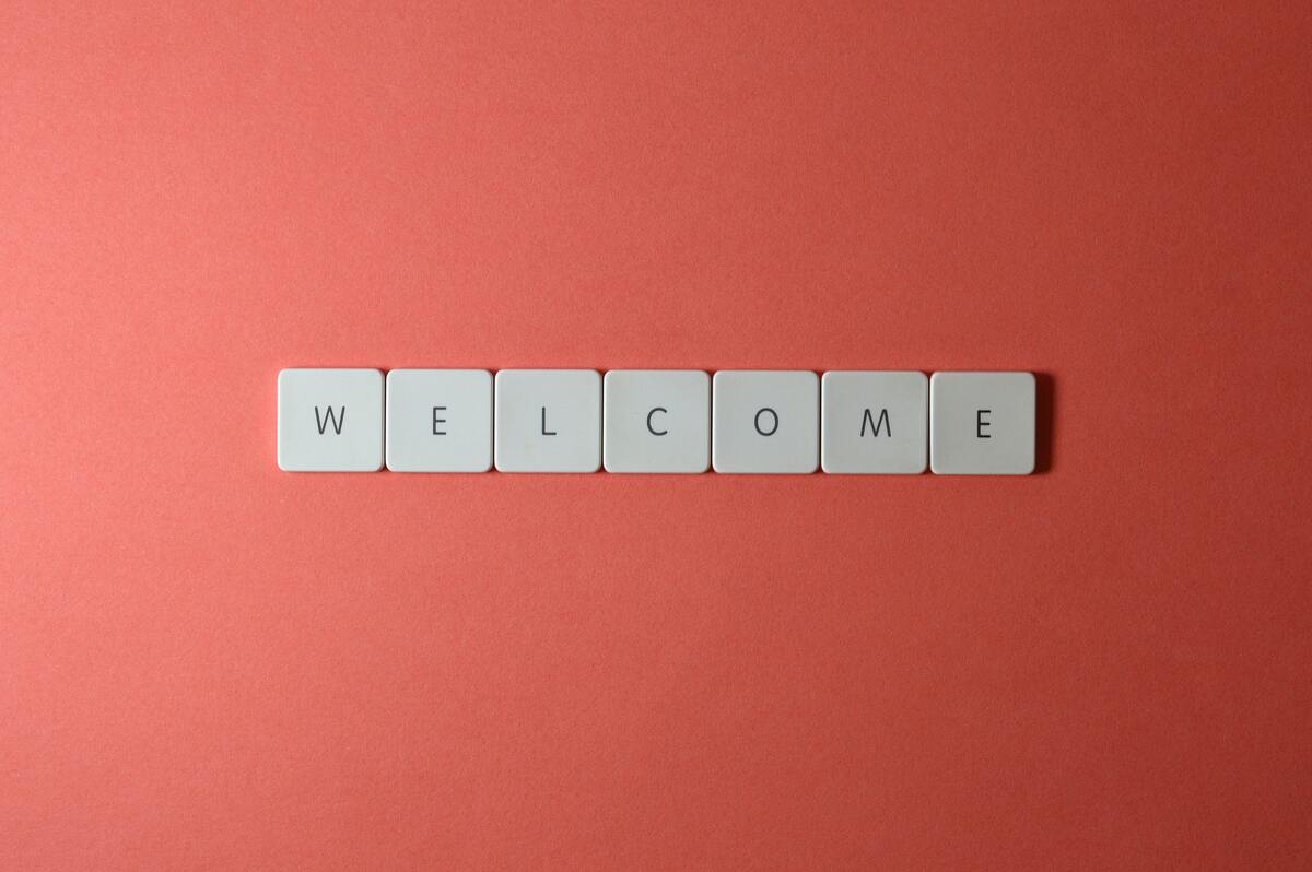 White letter tiles spell out "welcome" against a red surface