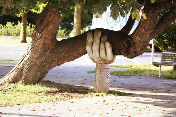 Carved wooden hand holding up large tree branch