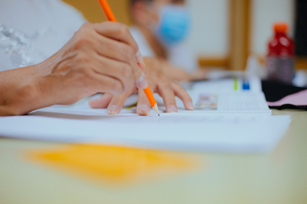 Close up on hand holding an orange pencil to paper